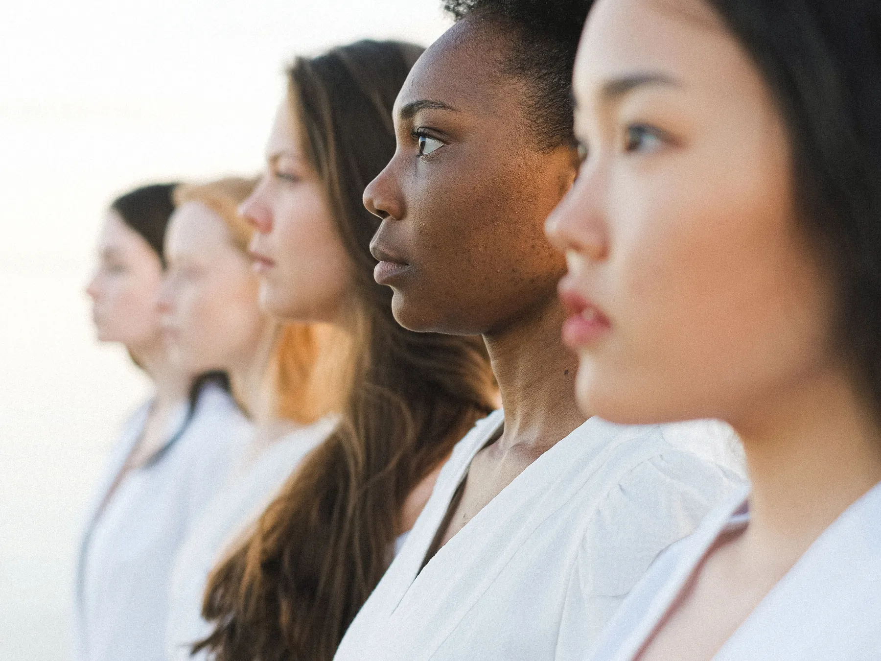 Cinq femmes d'origines diverses, de profil et côte à côte, dans une lumière douce et chaleureuse.