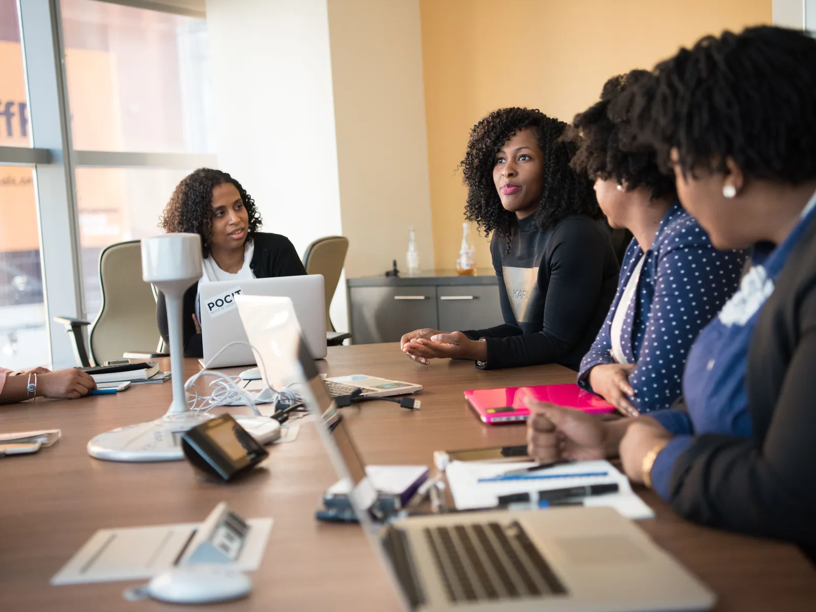Plusieurs femmes réunies autour d’une table de réunion avec ordinateurs portables et documents, dans un bureau lumineux.